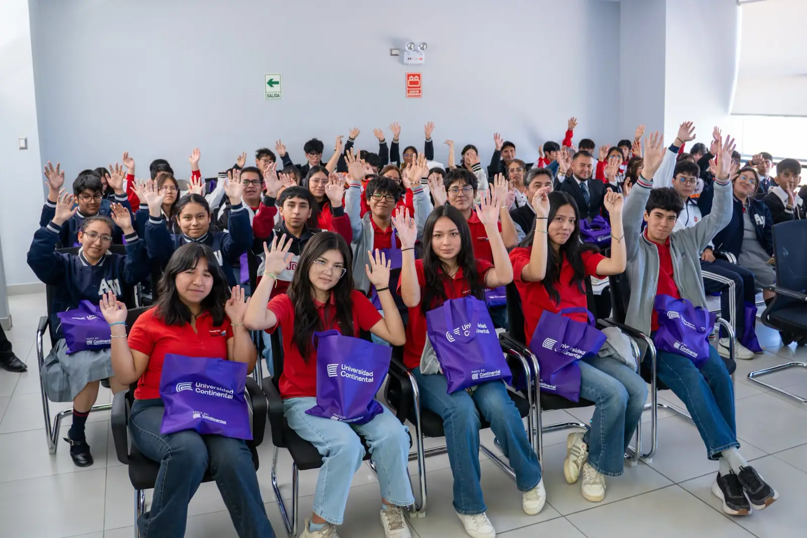 Escolares levantando la mano con bolsas de la Universidad Continental
